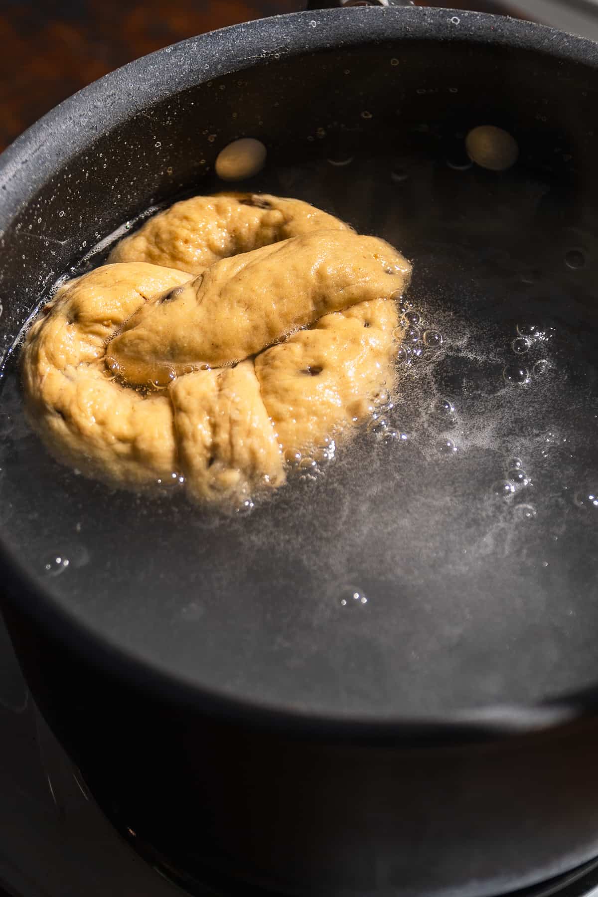 Pumpkin soft pretzel boiling in a baking soda bath.