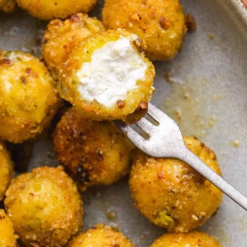 Fried goat cheese balls on a plate with a bite taken out of one.