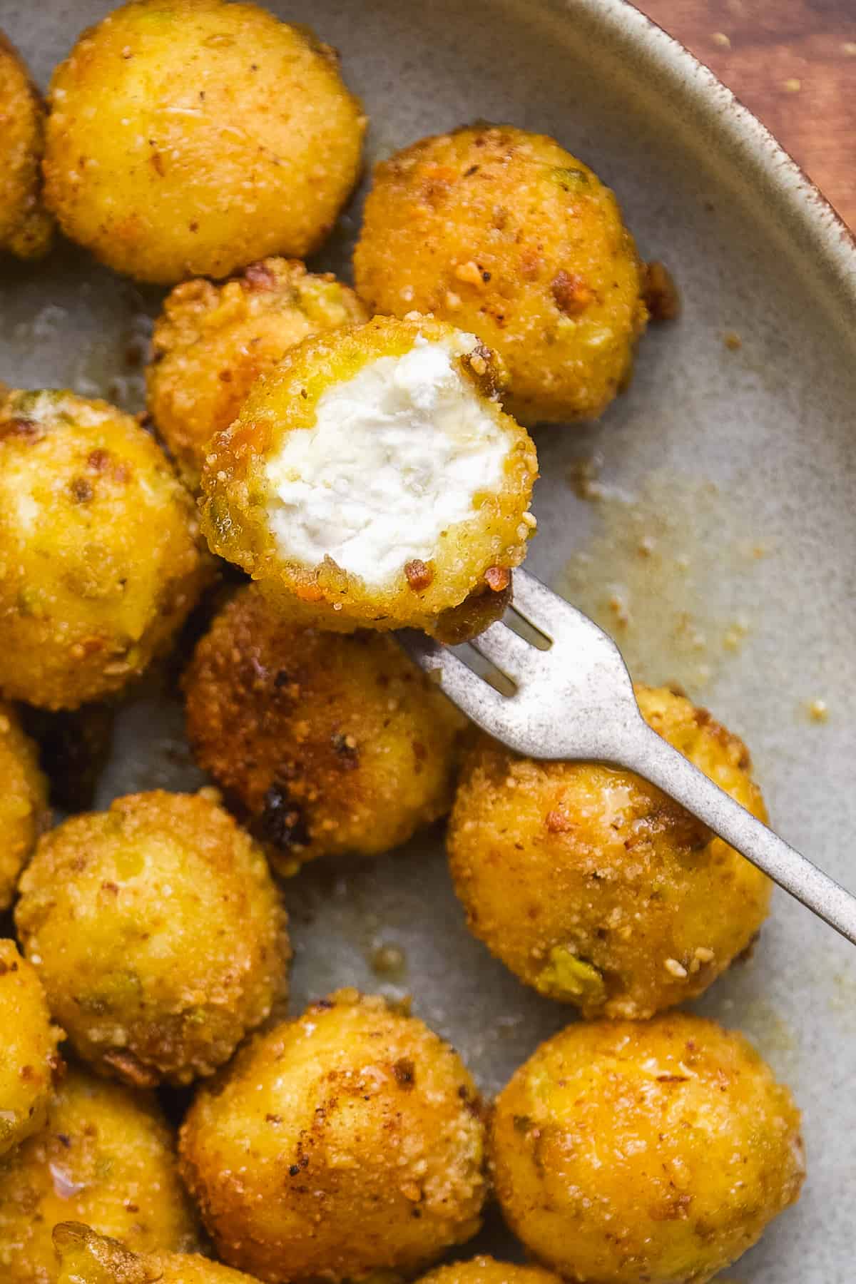 Fried goat cheese balls on a plate with a bite taken out of one.