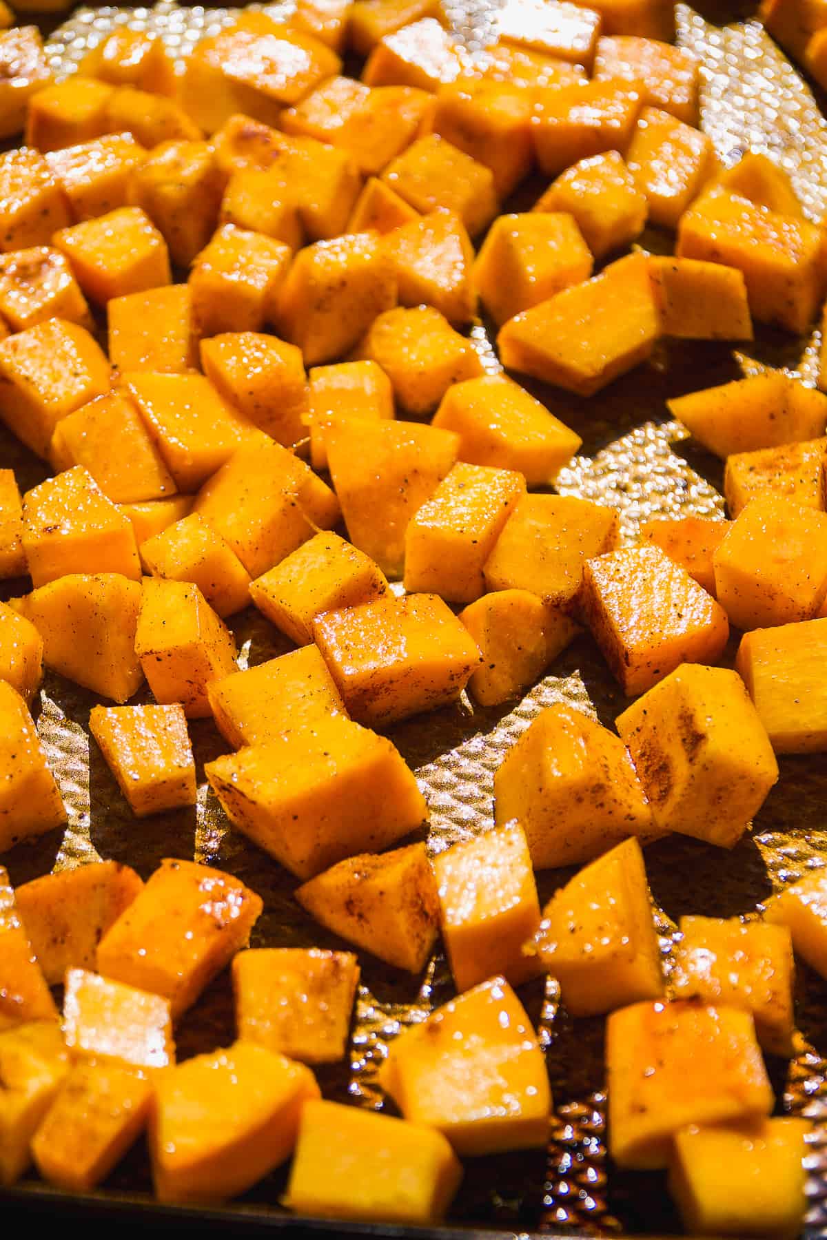 Pumpkin cubes tossed in spices and oil on a baking sheet.