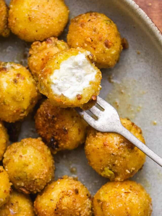 Fried goat cheese balls on a plate with a bite taken out of one.