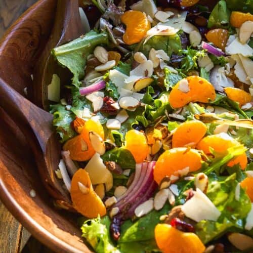 Mandarin orange salad tossed in wooden bowl on a wooden surface.