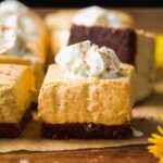 Pumpkin cheesecake bar on parchment paper with whipped cream.