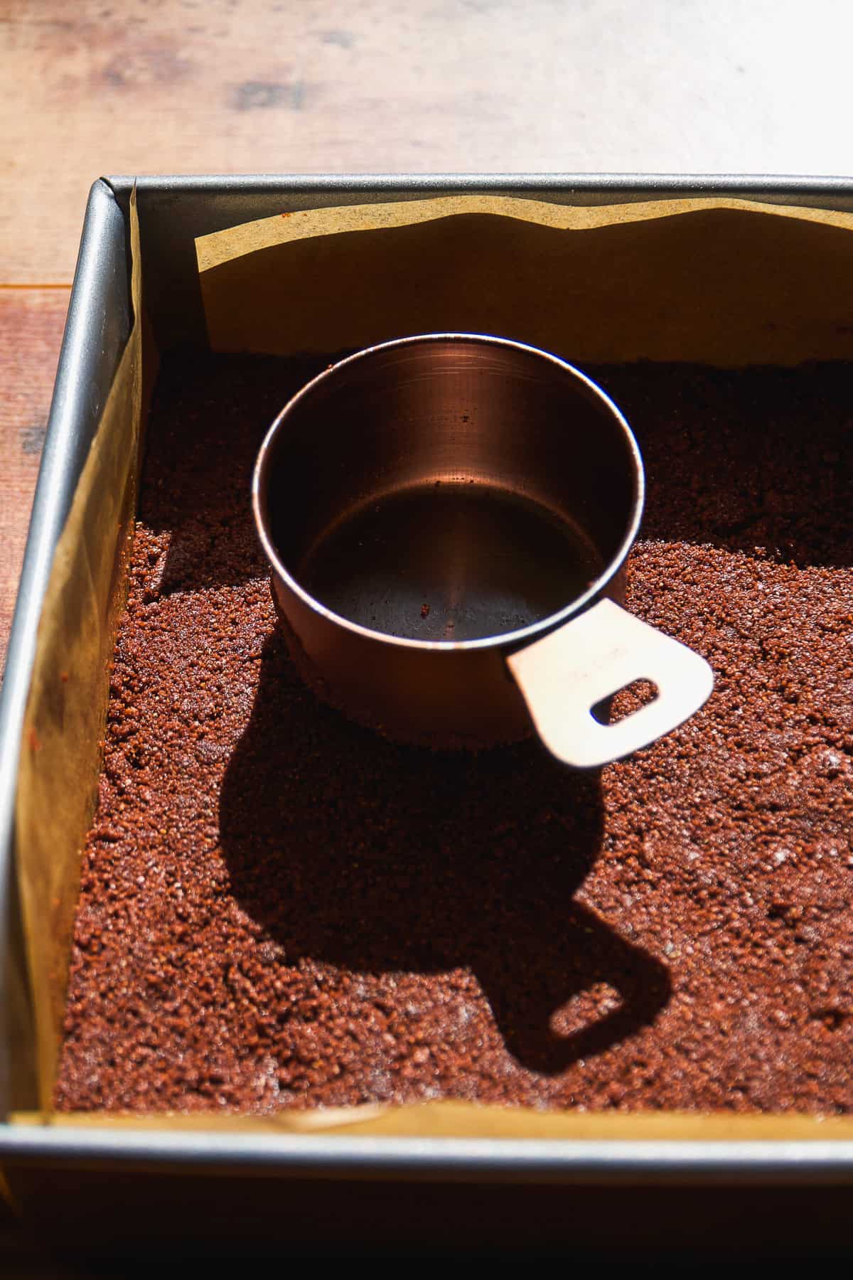 Cookie crust being packed down into a square pan.