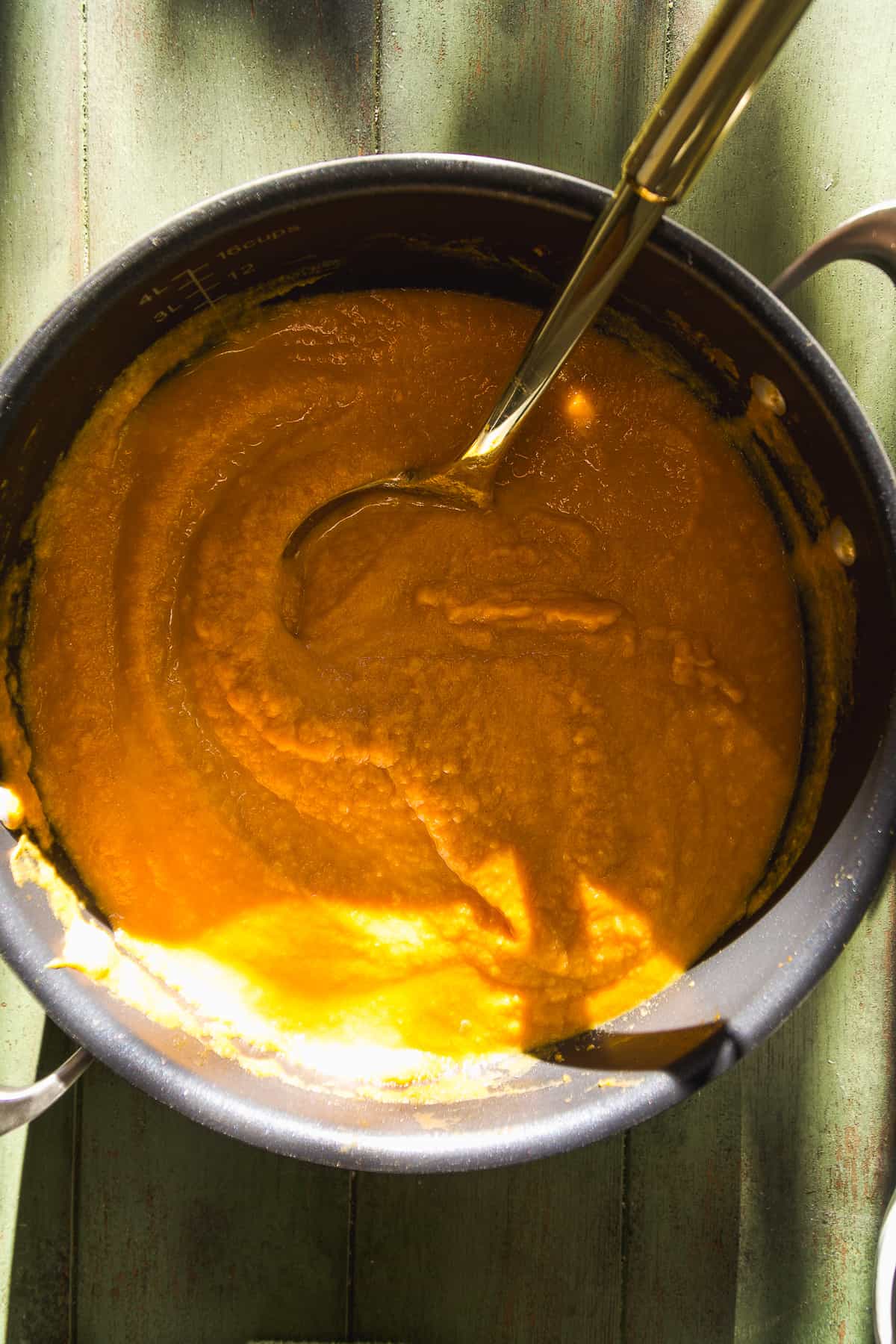 Pot of pumpkin sweet potato soup on green surface.