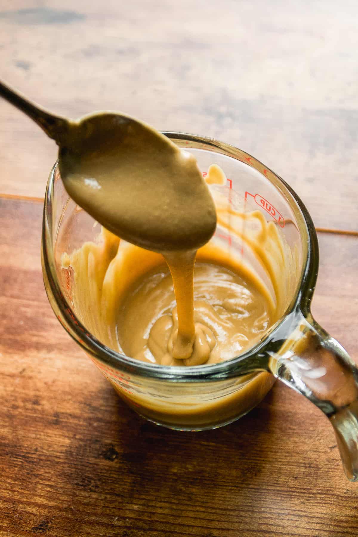 Tahini sauce dripping off a spoon into a glass.