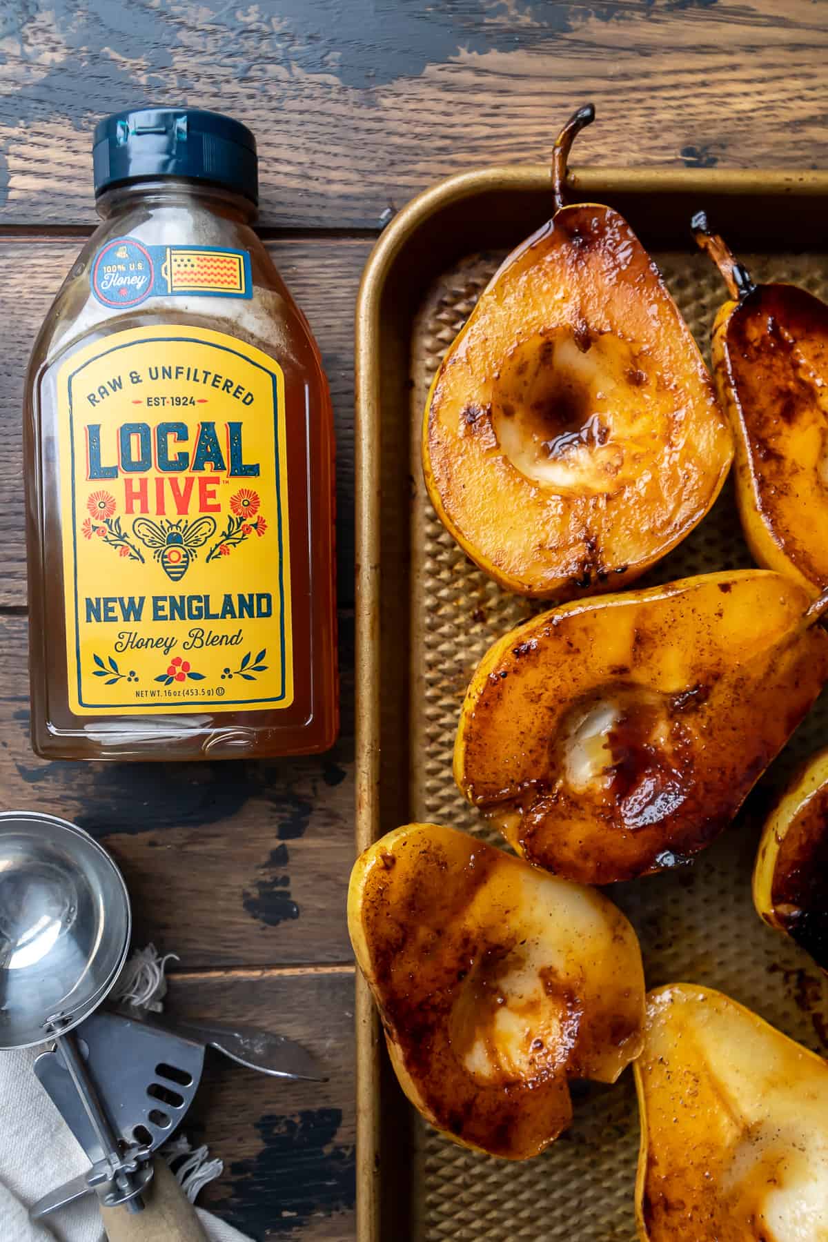 Caramelized pear halves on a baking sheet with a jar of honey.