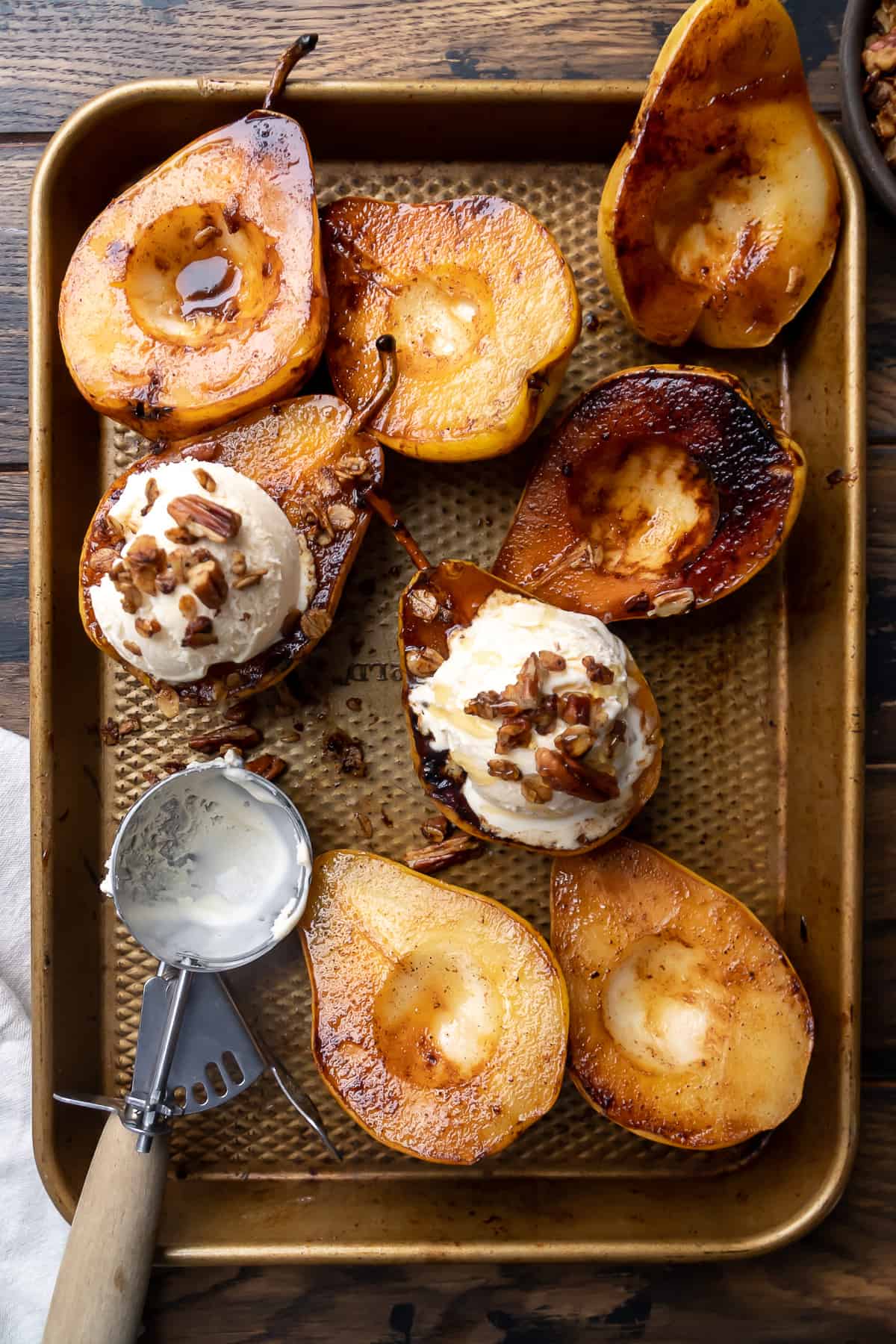 Caramelized pears on a baking pan with ice cream on top.