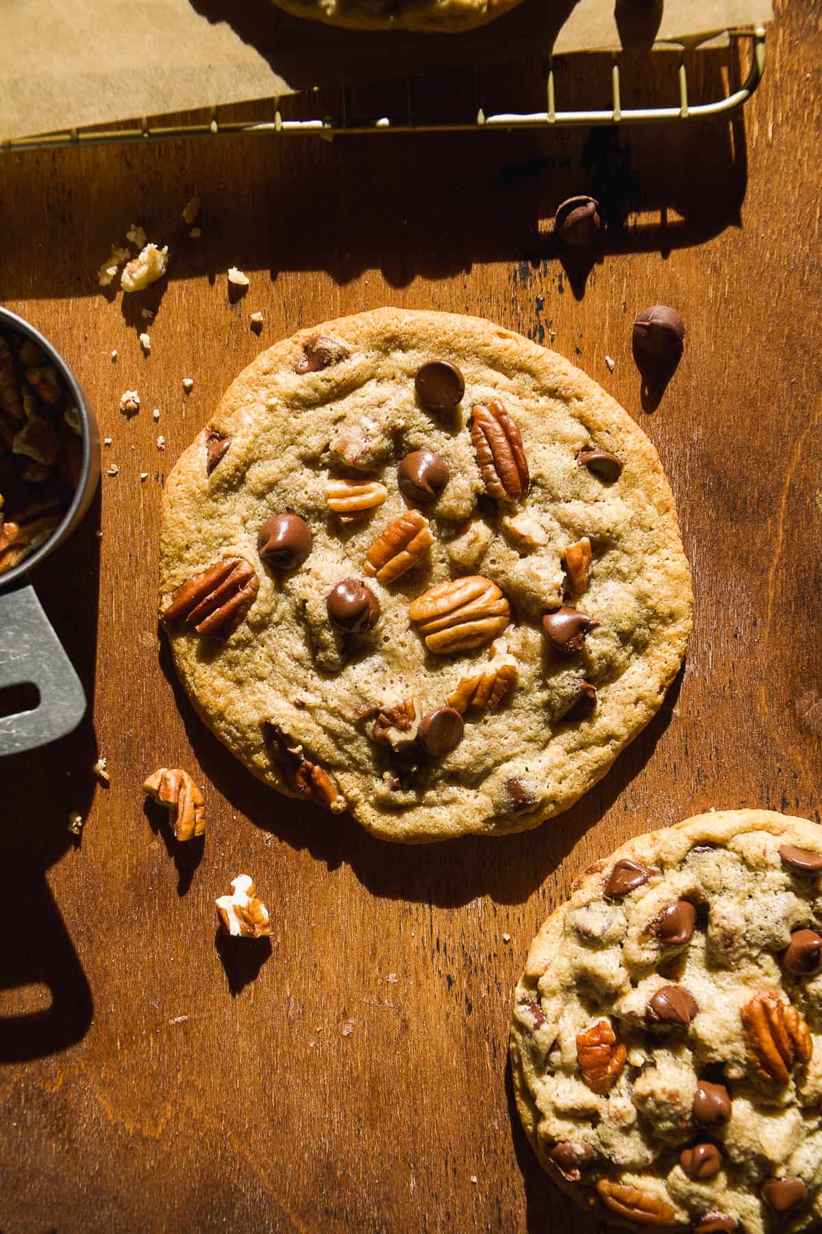 Chocolate chip pecan cookies on wooden surface with chocolate and pecans.