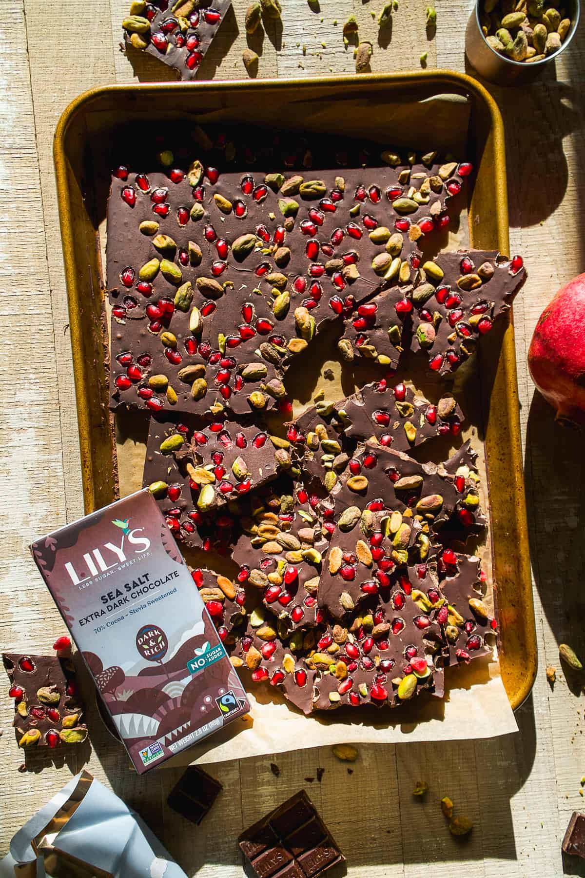 Overhead view of chocolate bark on a baking sheet with pomegranates and pistachios.