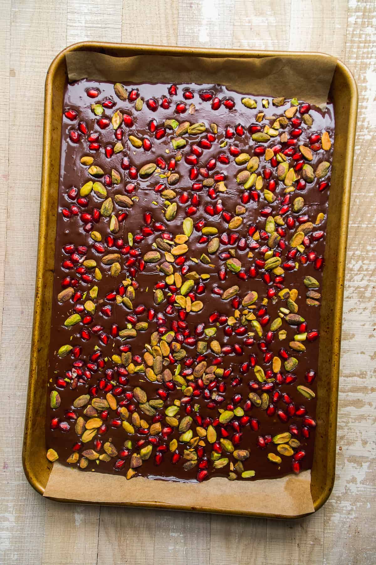 Melted chocolate on a baking sheet with pomegranates and pistachios on top.