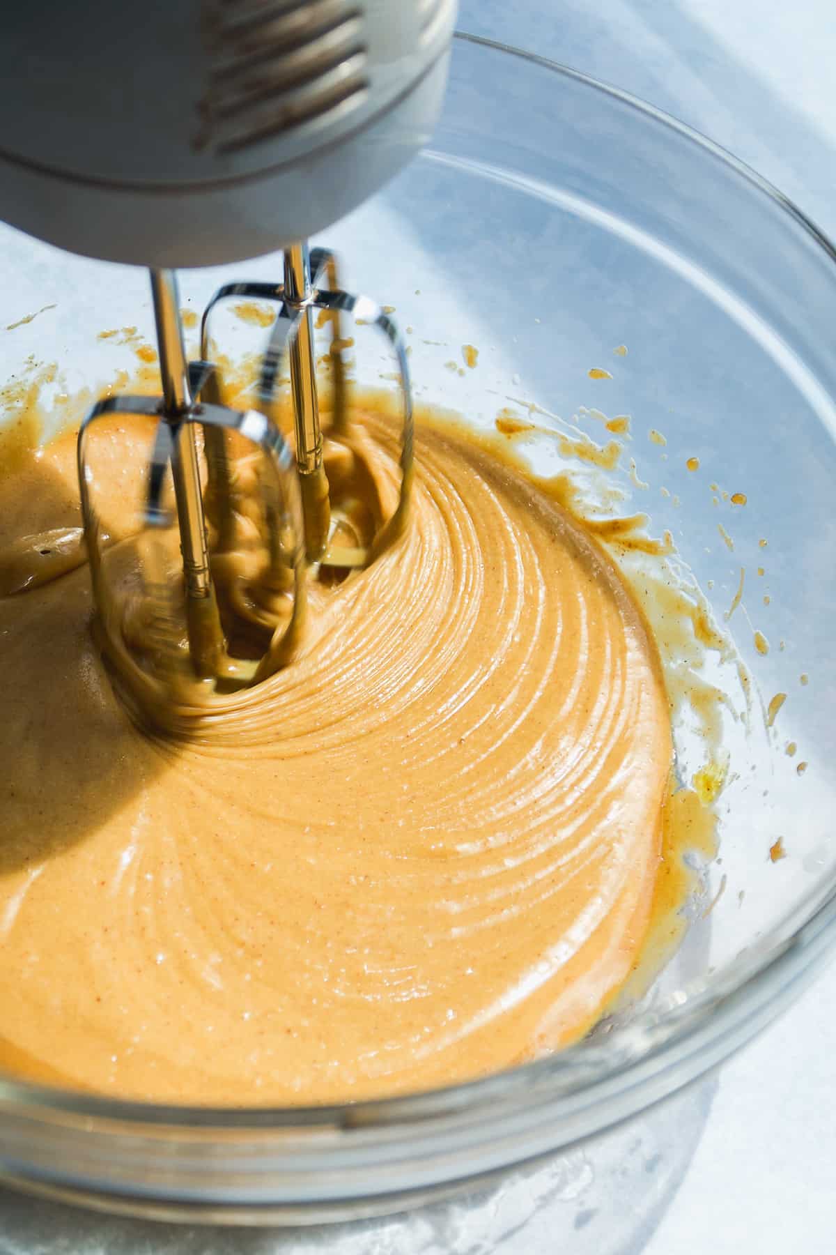 Mixer mixing peanut butter cookies in a glass bowl.