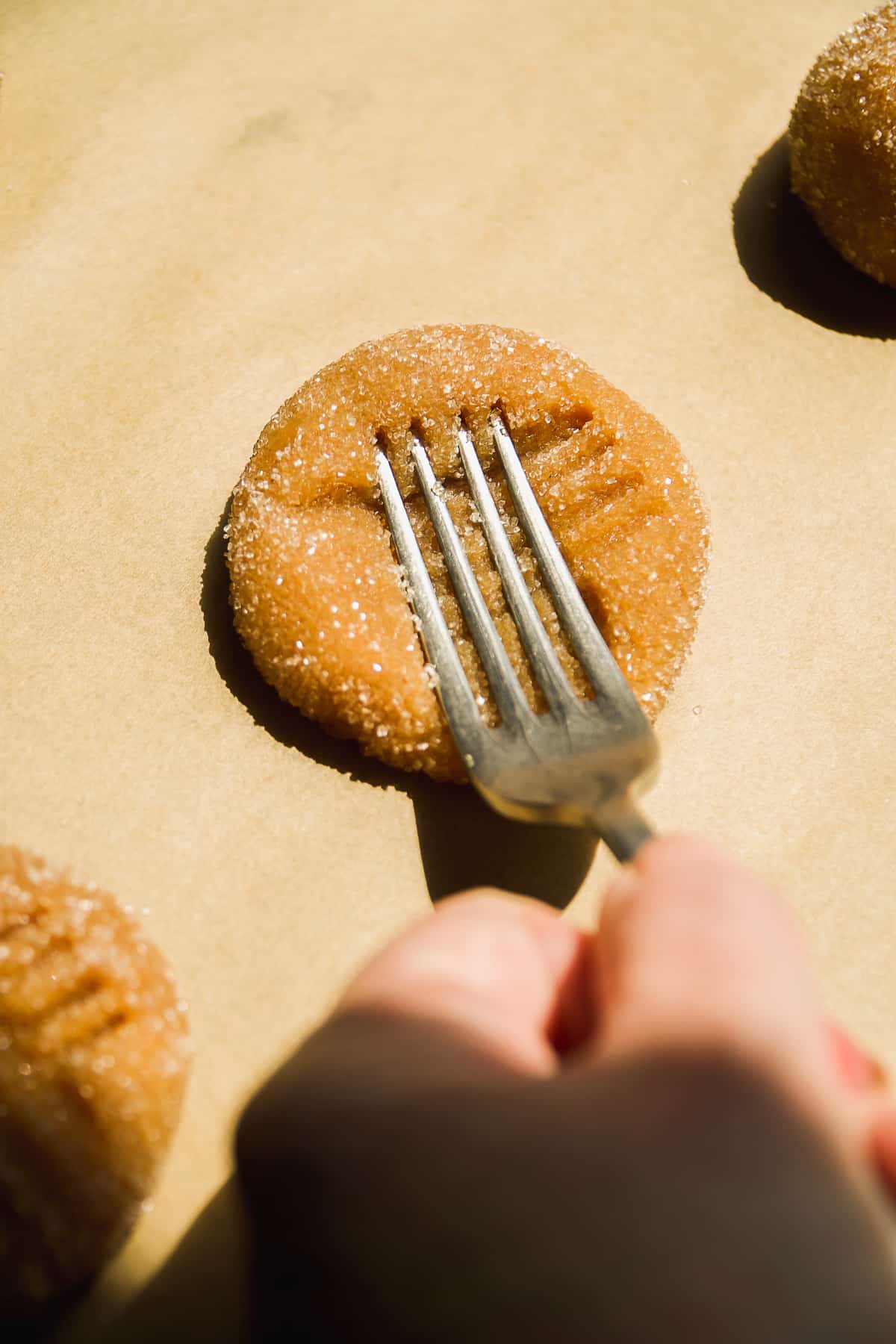 Person pressing the back of a fork into a peanut butter almond flour cookie dough ball.