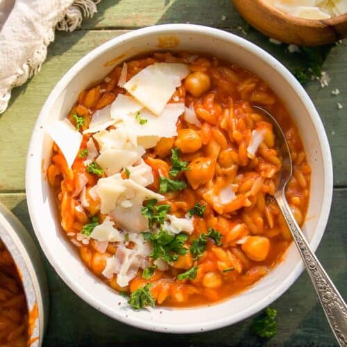 Chickpea soup in a bowl with cheese and a spoon resting inside.