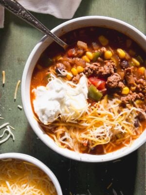 Sweet chili in a white bowl with cheese and yogurt on top.