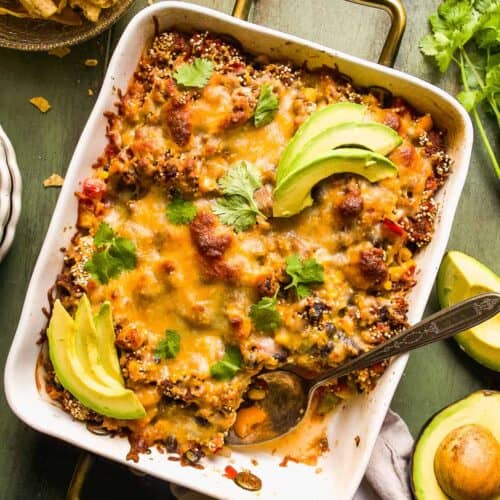 Taco casserole on a green surface with avocado slices.