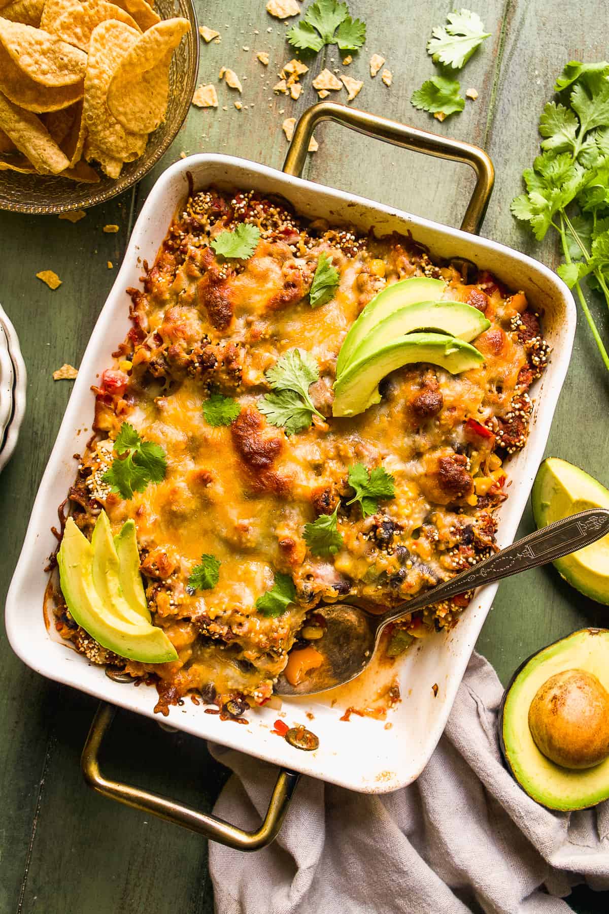 Taco casserole on a green surface with avocado slices.