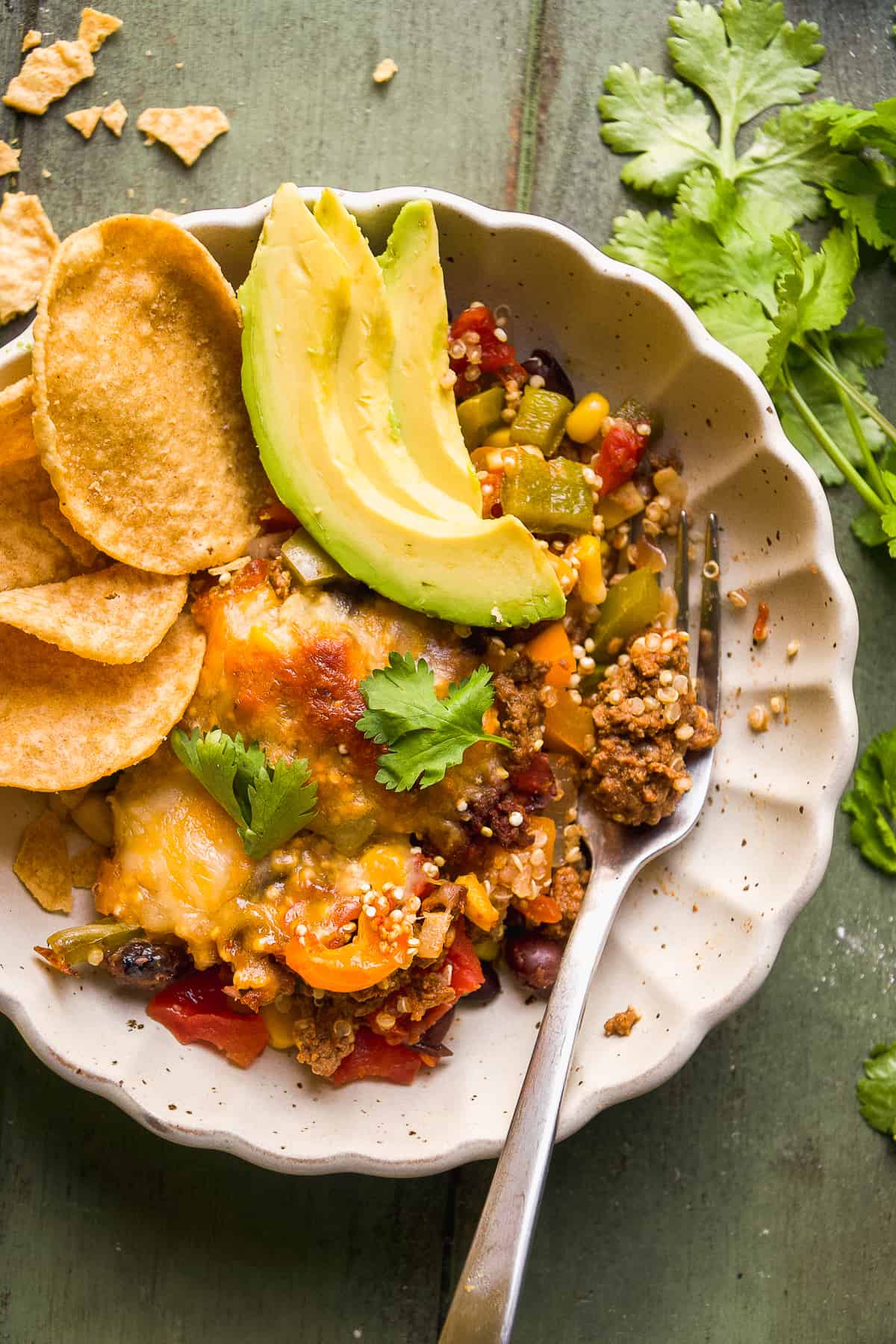 Taco casserole in a bowl with chips and avocado slices.