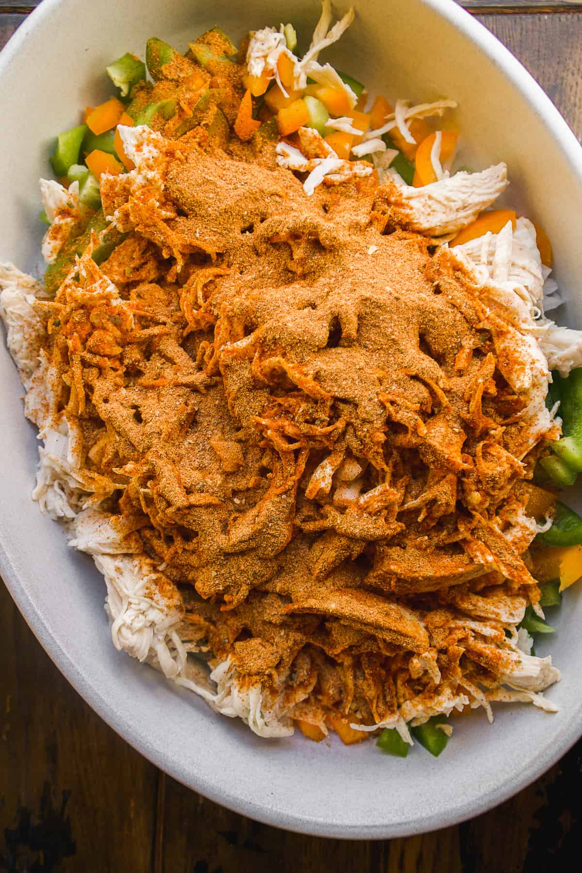 Pulled chicken and veggies about to mixed with taco seasoning in a large dish.