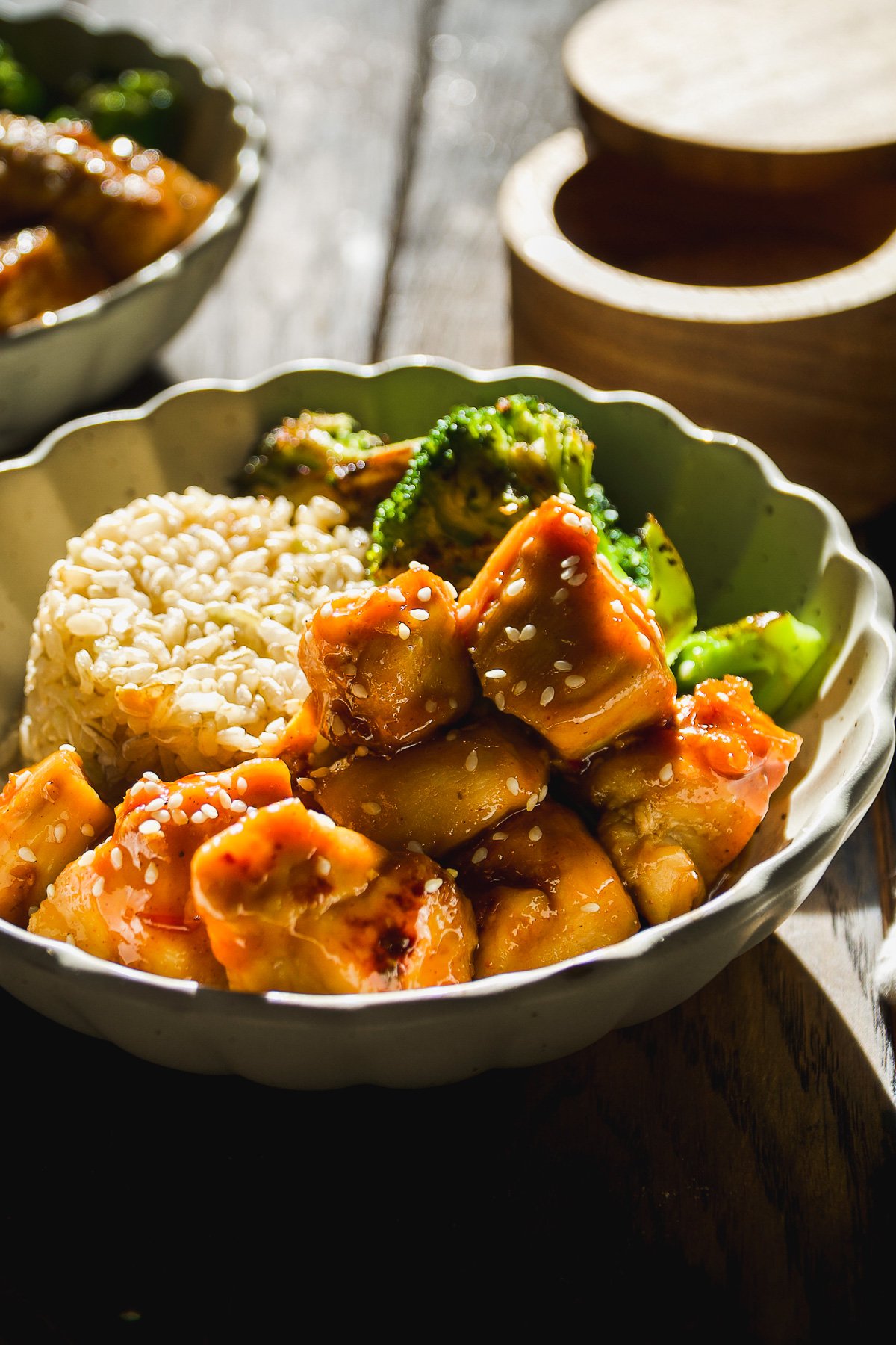 Side view of a bowl with honey, sesame, chicken, rice, and broccoli.