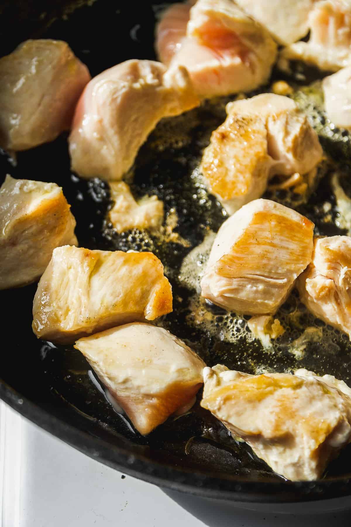 Chicken breast cut into pieces cooked in a black skillet.