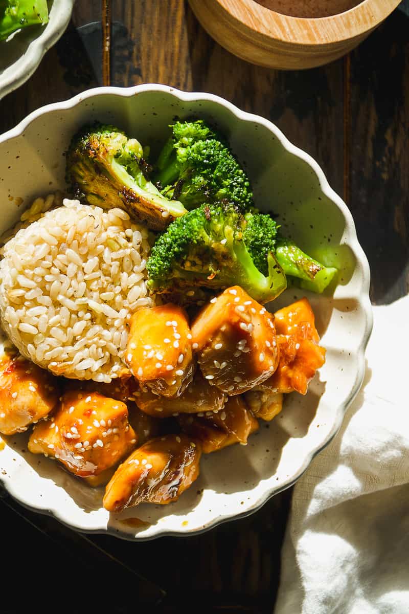 Honey sesame chicken in a bowl with rice and broccoli.