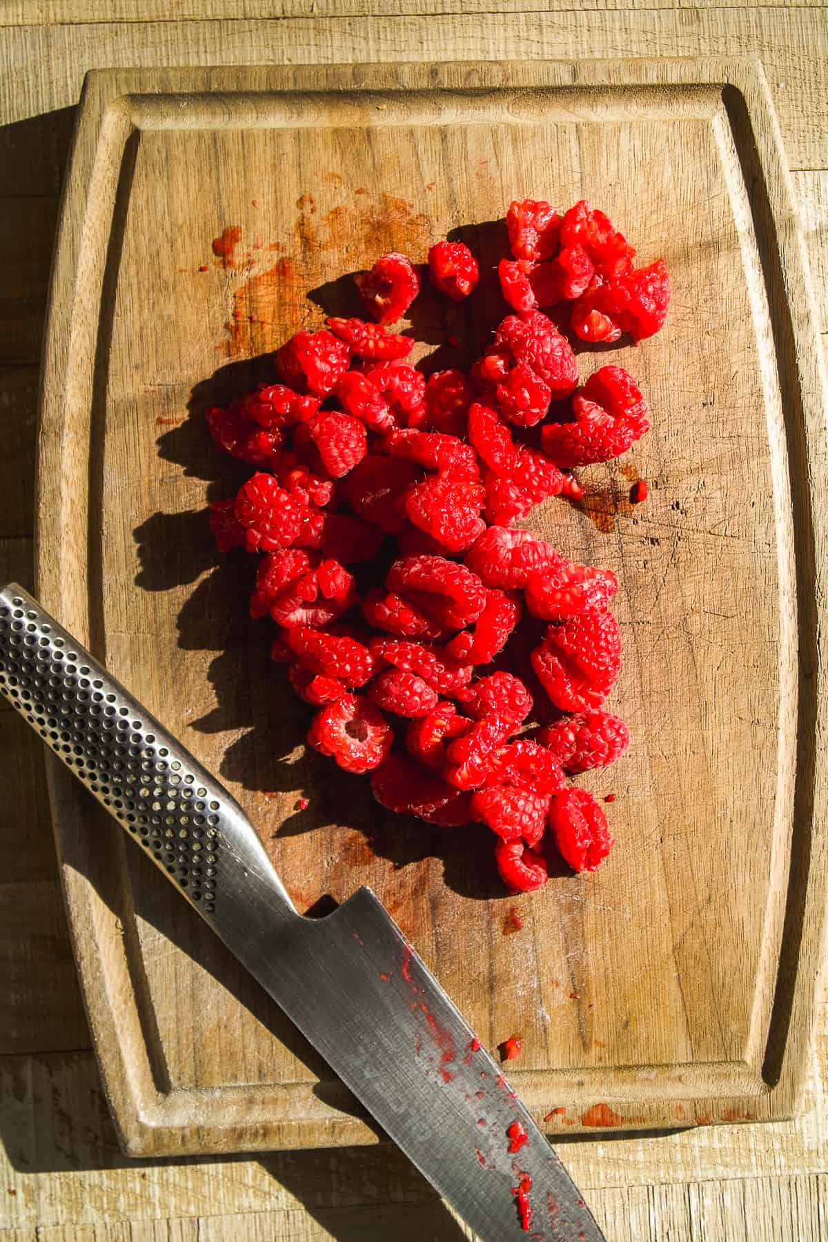 Raspberries cut into pieces on a wooden cutting board.