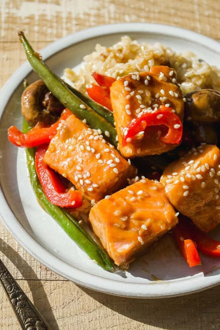 Salmon stir fry with vegetables and sesame seeds on a white plate.