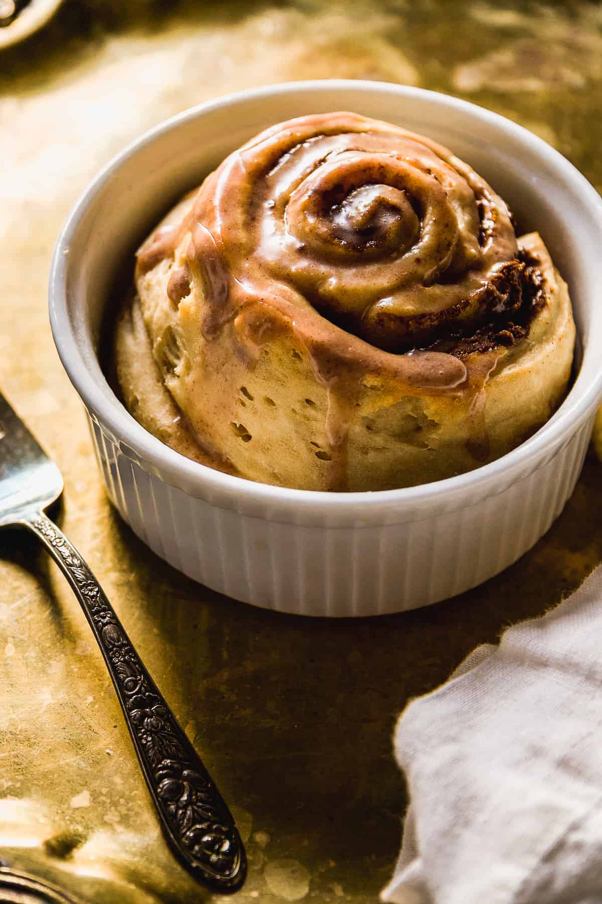 Single serve cinnamon roll in a ramekin on a gold platter.