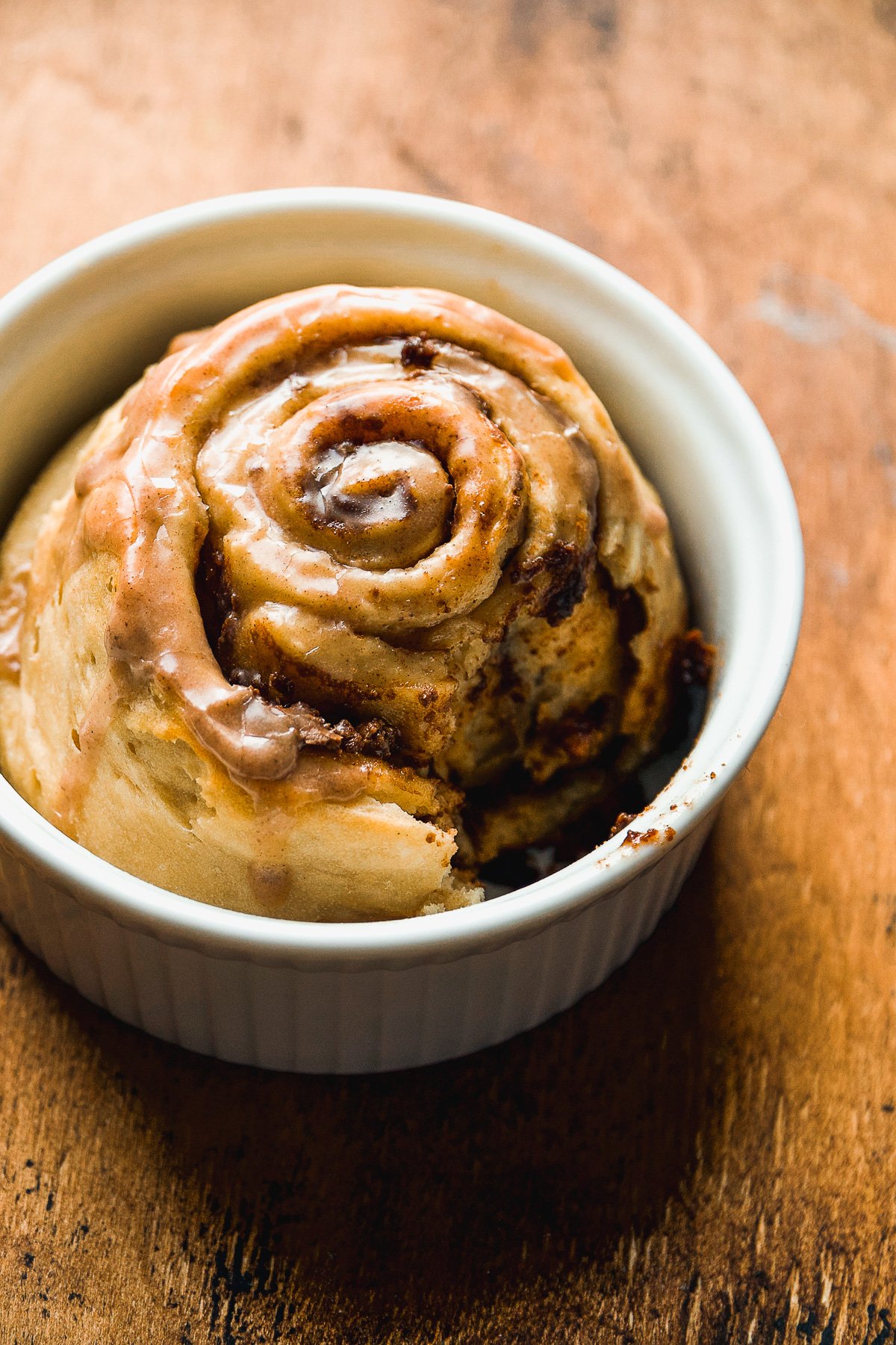 Single serve cinnamon roll in a ramekin with a bite taken out of it.