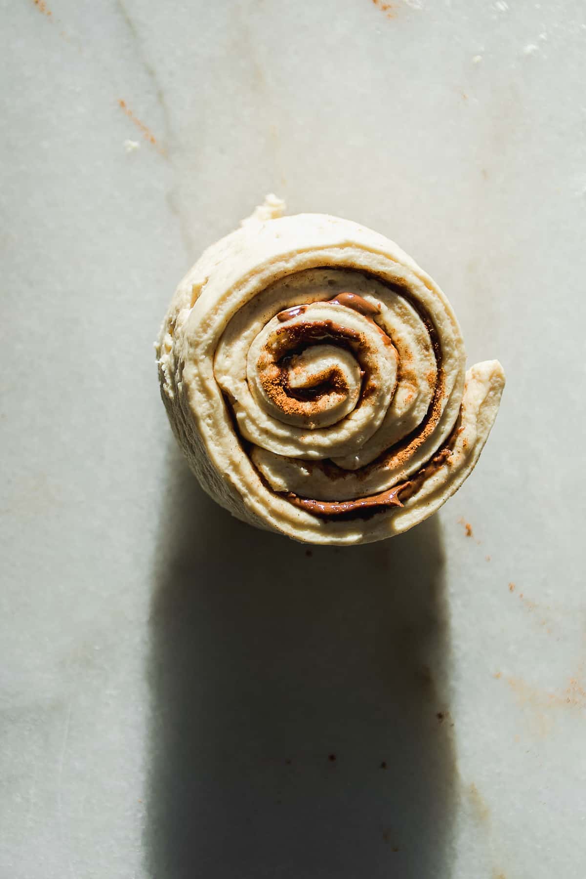 Large cinnamon roll about to be baked on a marble surface.