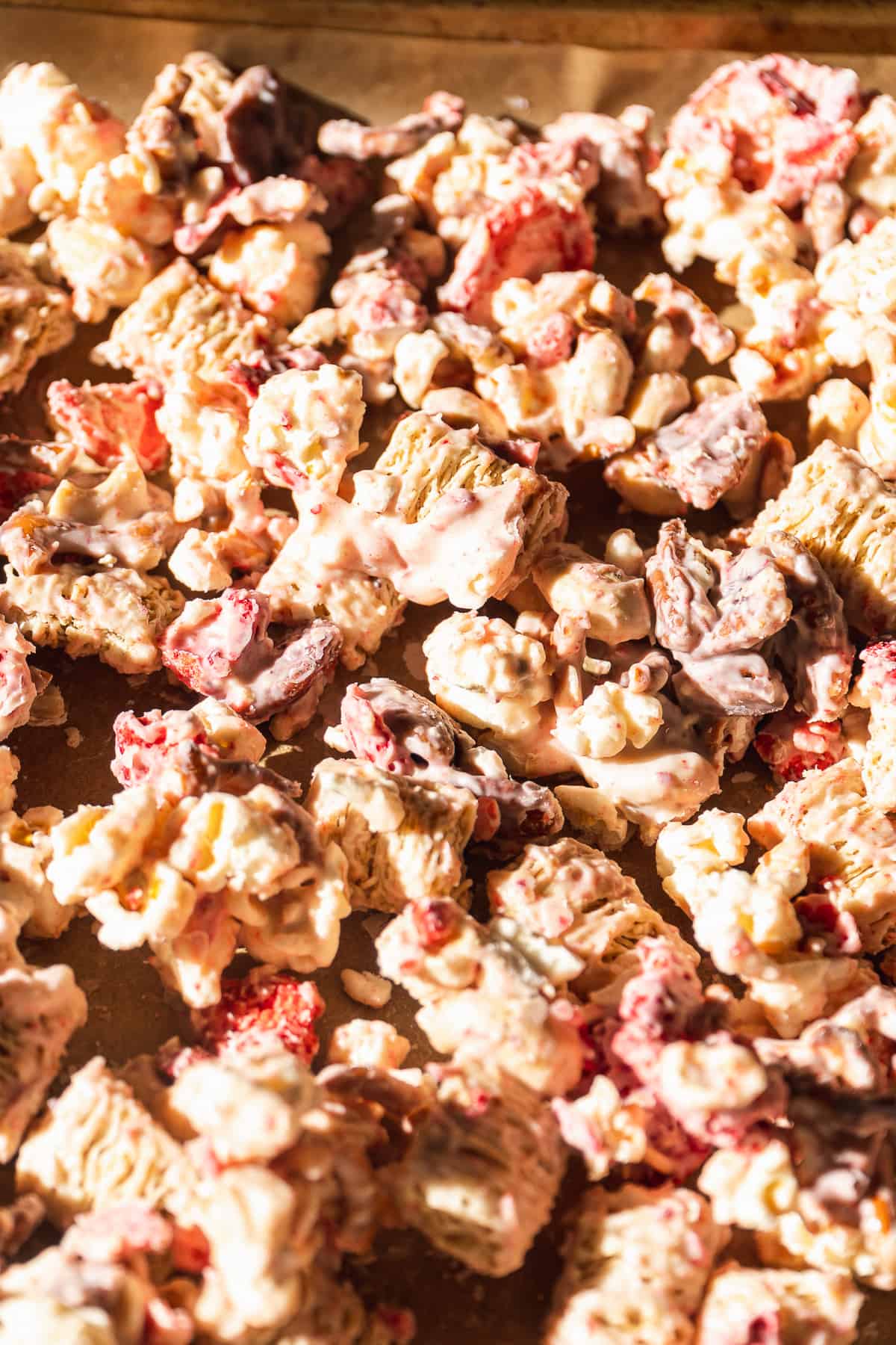 White chocolate strawberry coated cereal and mix ins on a baking pan.