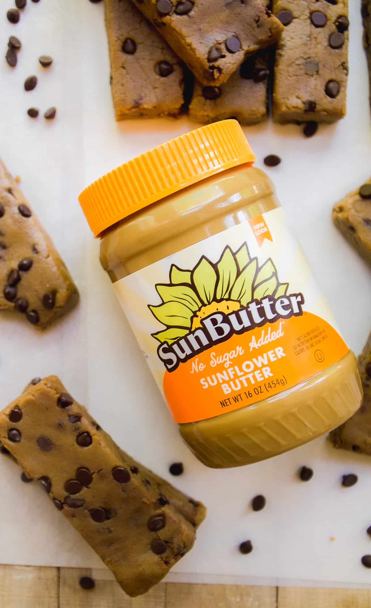 Jar of sunflower butter with orange lid and cookie dough protein bars on the surface.