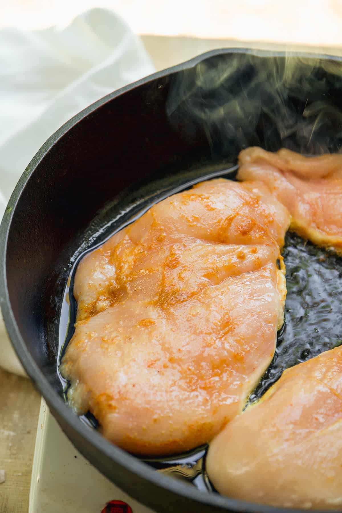 Chicken breast cooking in a cast iron skillet.