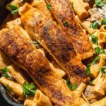 Salmon filets on top of creamy pasta in a cast iron skillet.