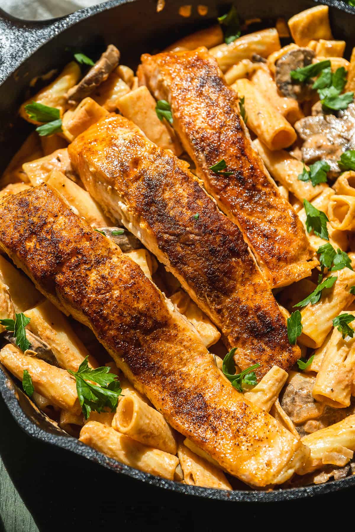 Salmon filets on top of creamy pasta in a cast iron skillet.