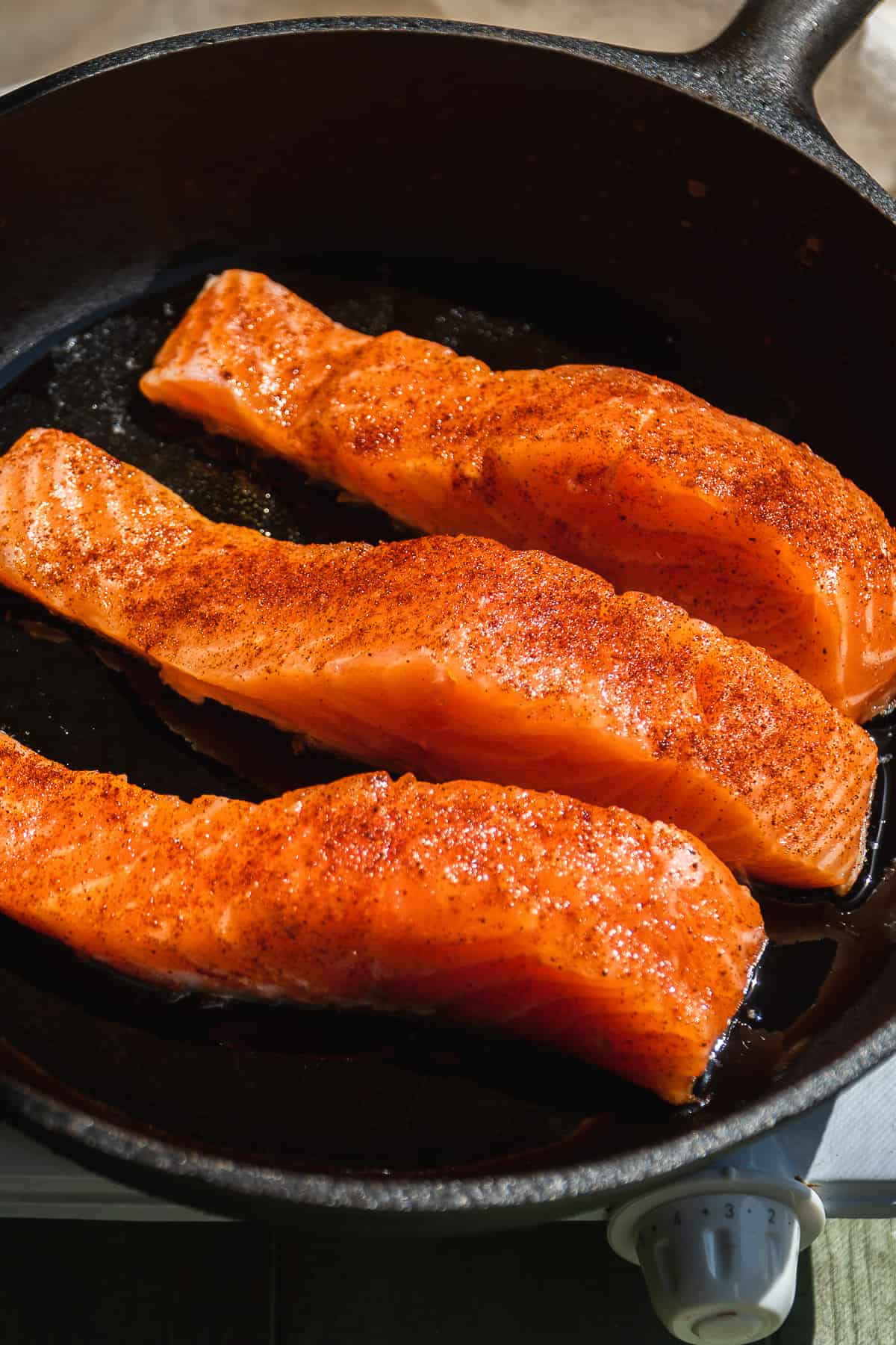Salmon filets cooking on a cast iron skillet.