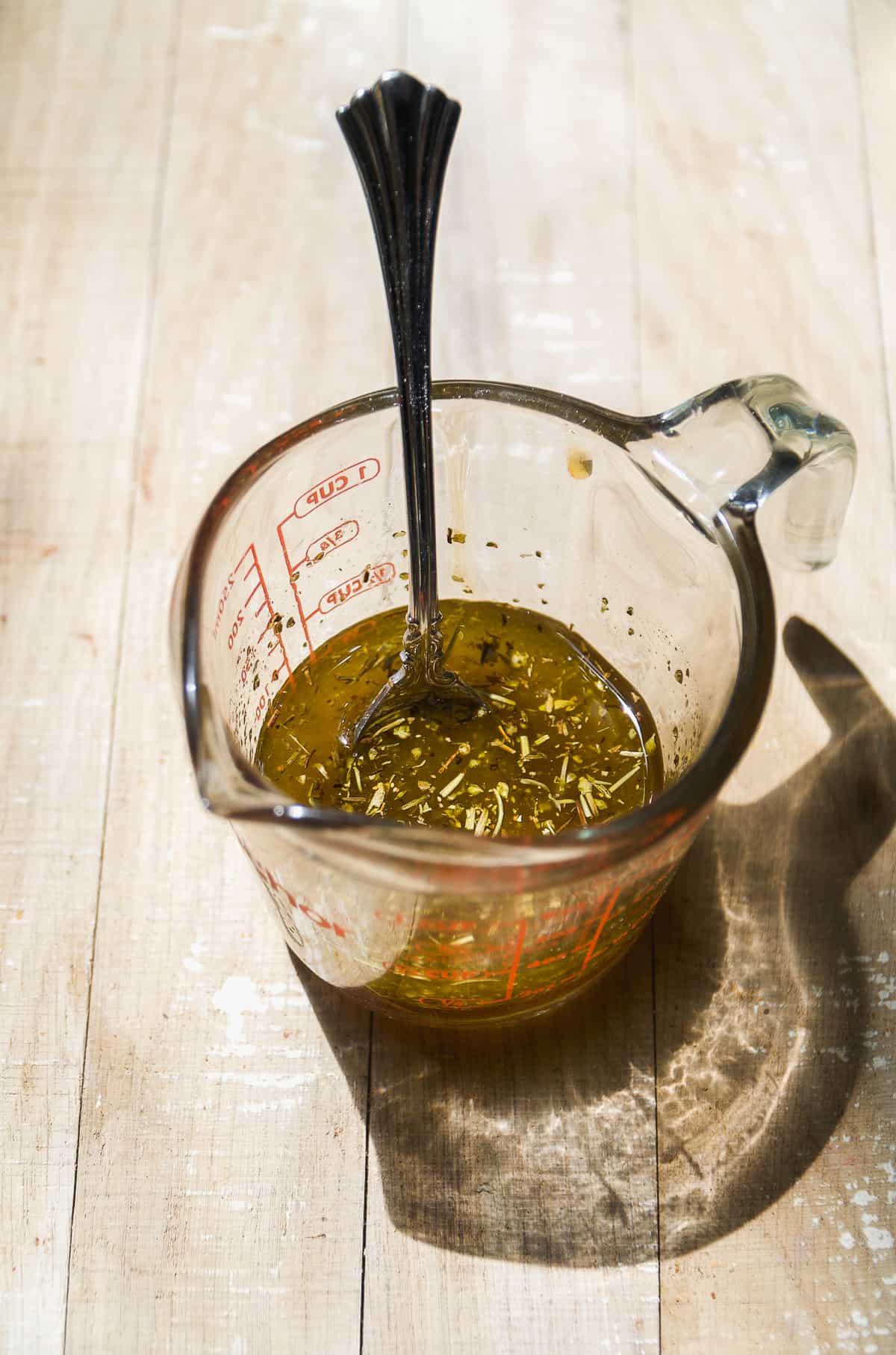 Glass measuring cup with italian dressing and a spoon inside.