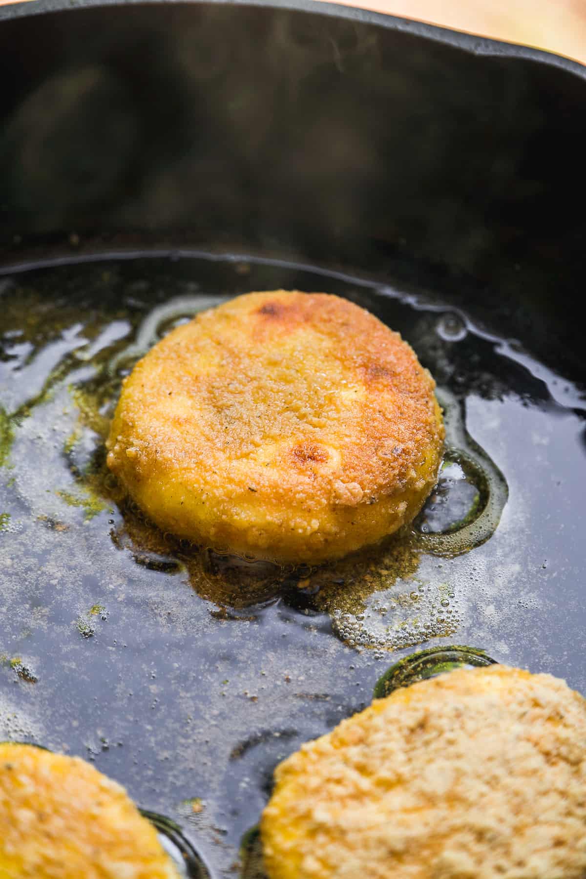Goat cheese patty pan frying in a cast iron skillet.