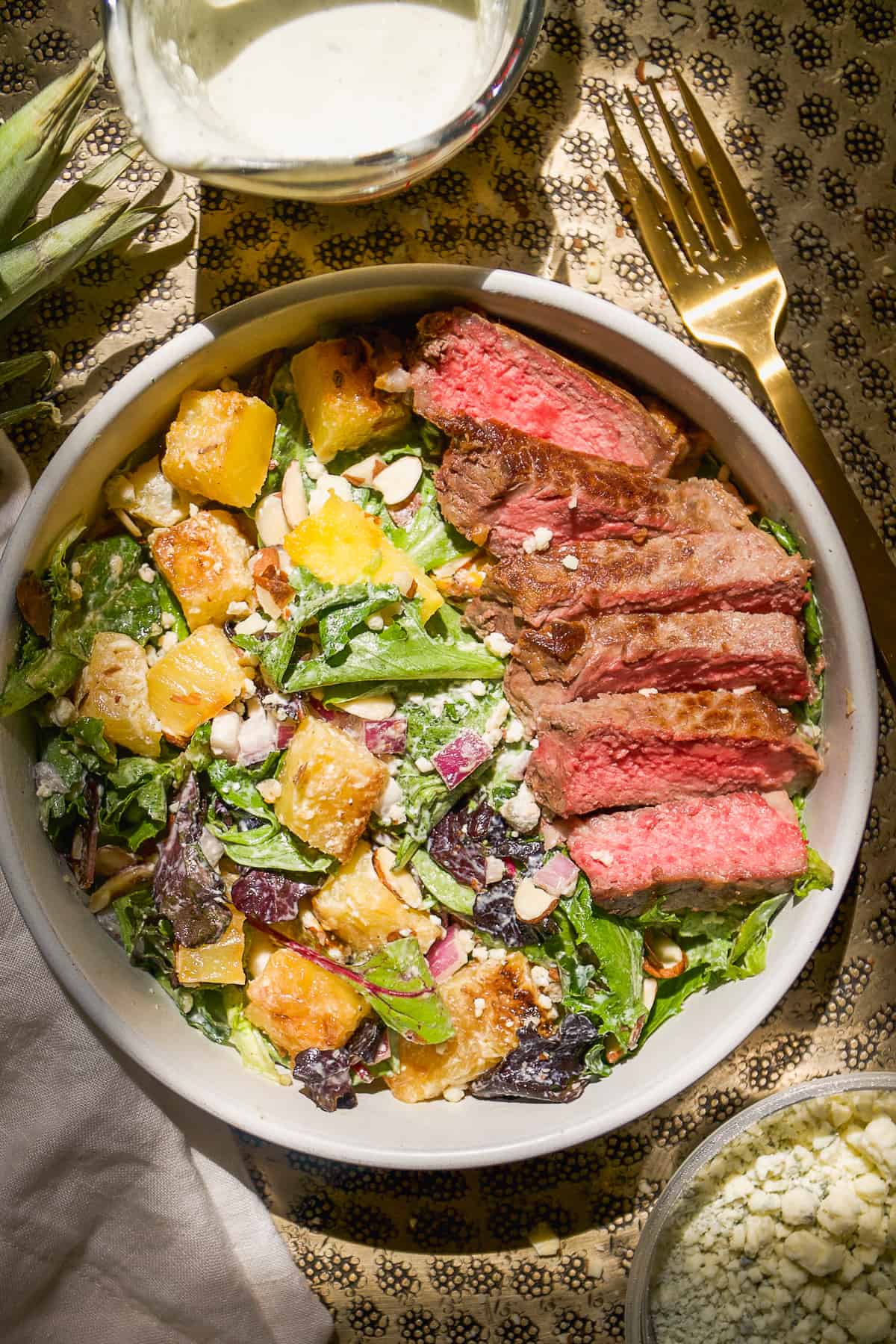 Overhead view of gorgonzola salad with strips of steak and pineapple on top.