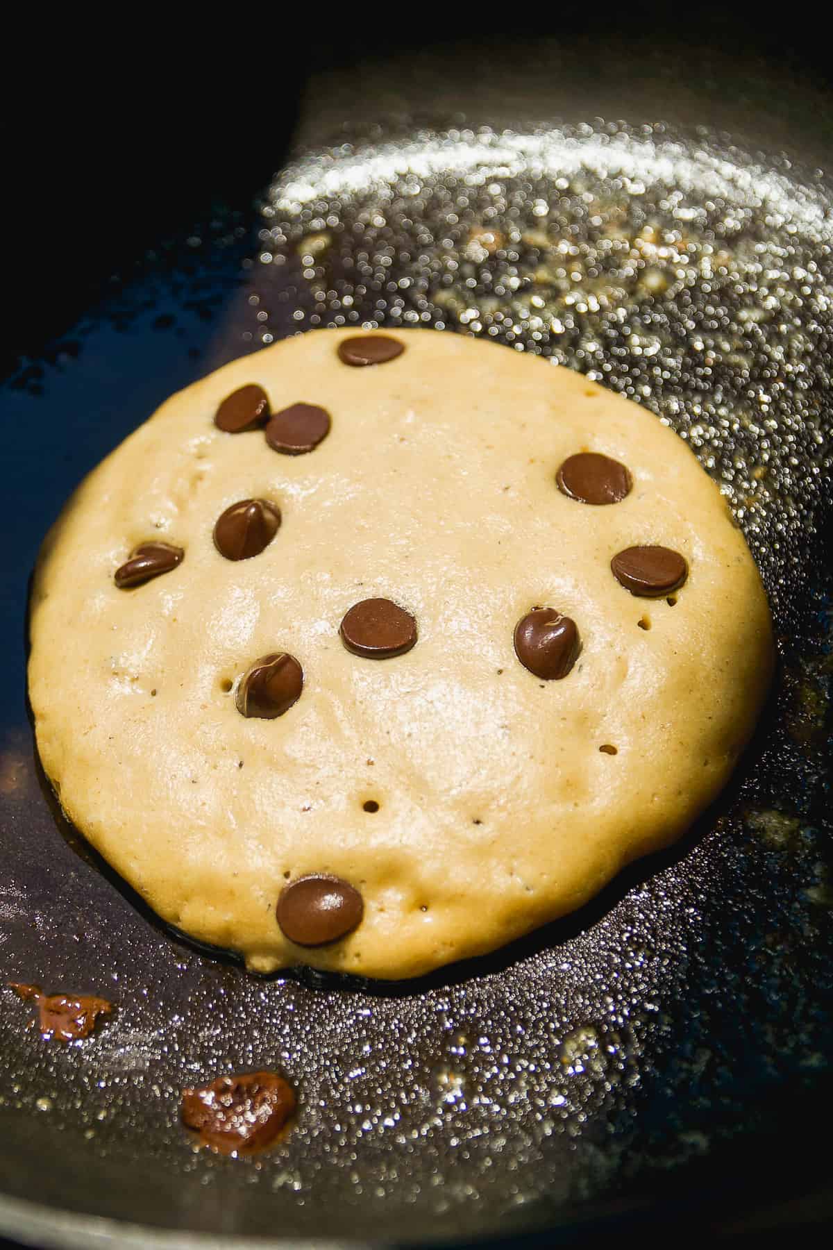 Chocolate chip oat flour pancake cooking on a skillet.