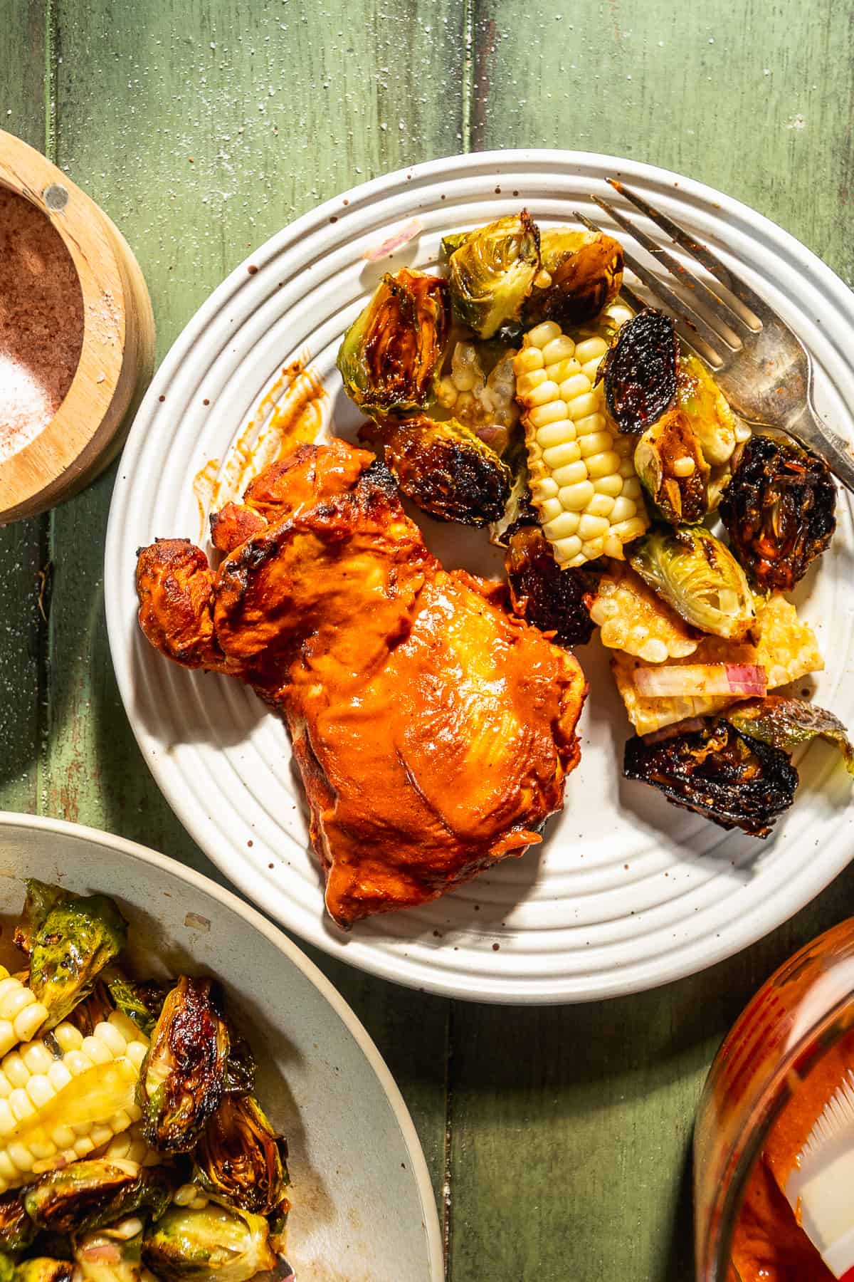 Baked bbq chicken thighs with corn and brussel sprouts on a white plate.