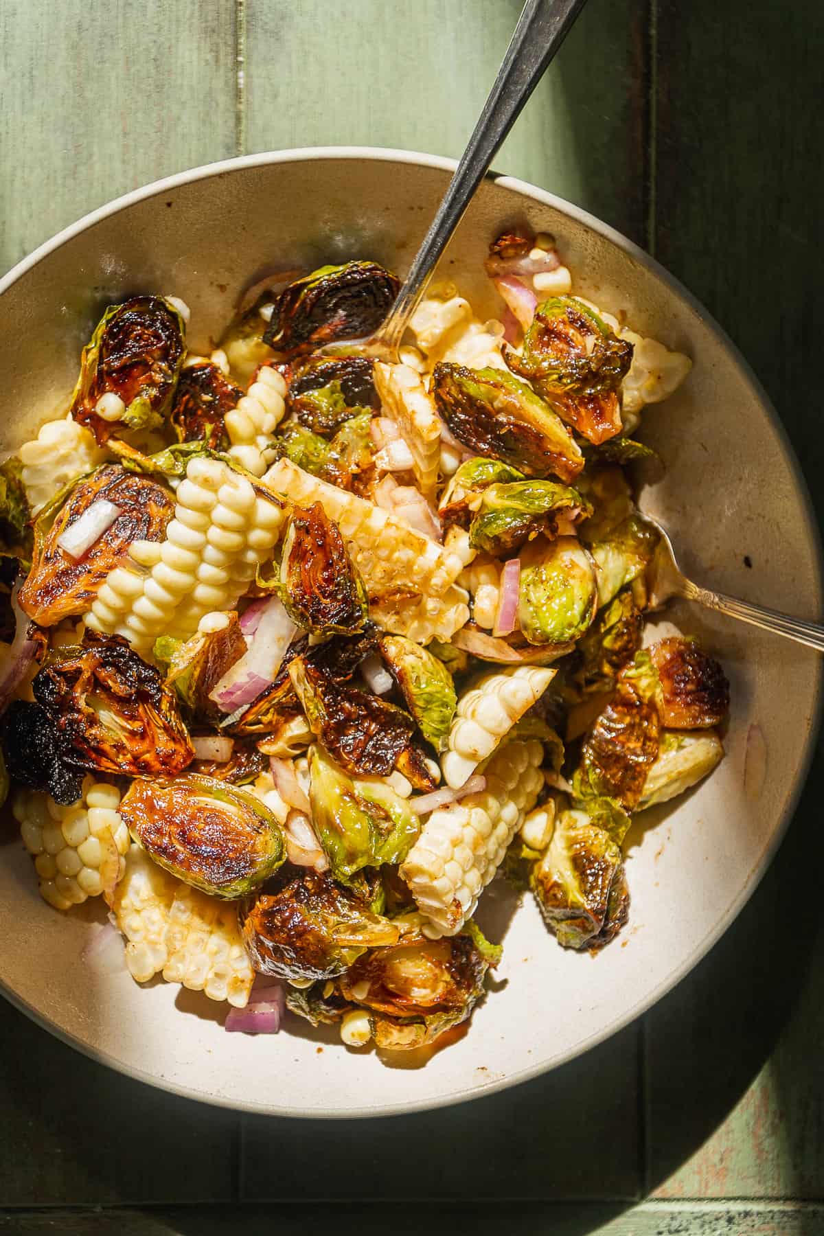 Bowl with brussel sprouts and corn on a green surface.