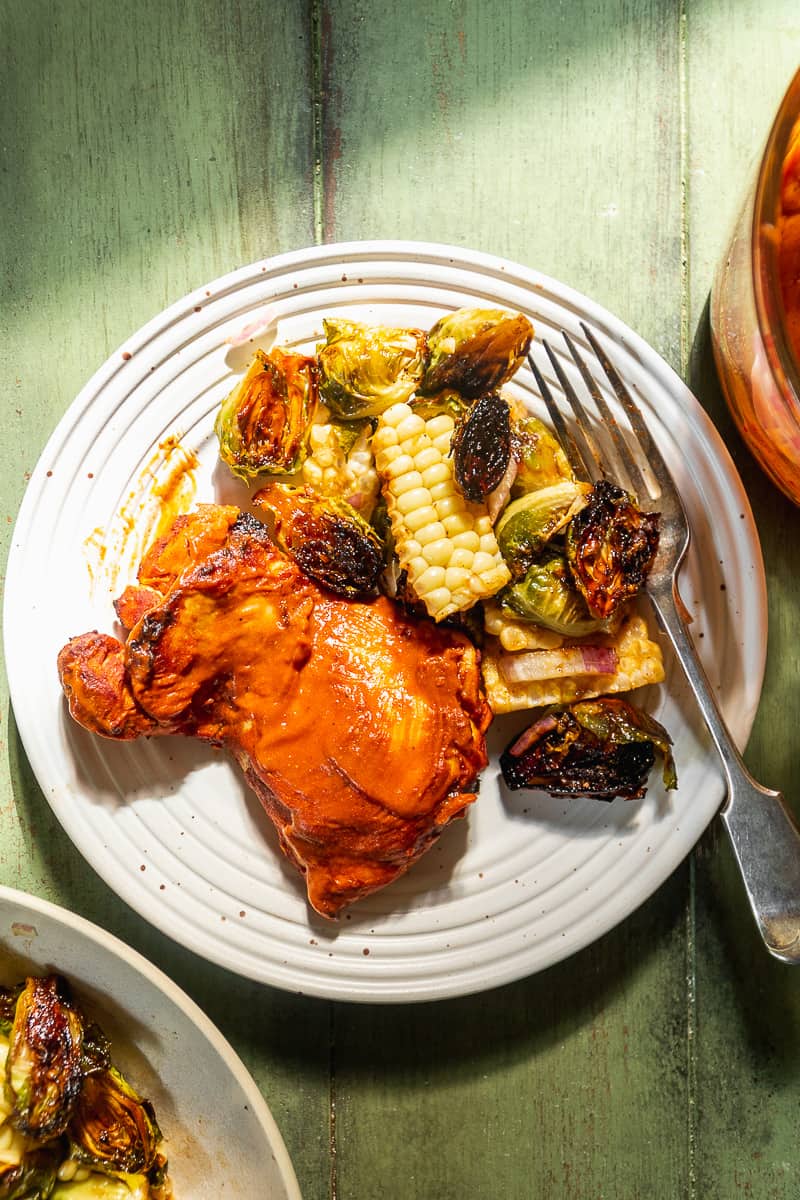 Baked bbq chicken thighs on a plate with brussel sprouts and corn.