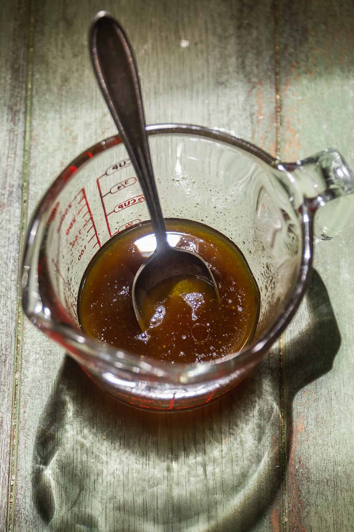 Oil and spices mixed in a measuring cup with a spoon.