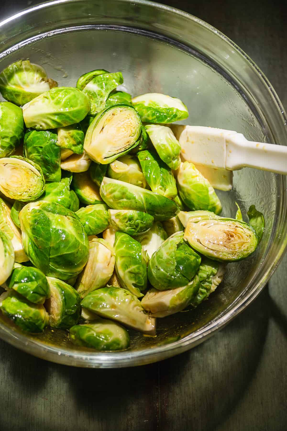 Brussel sprouts cut in half in a glass bowl tossed in oil and spices.