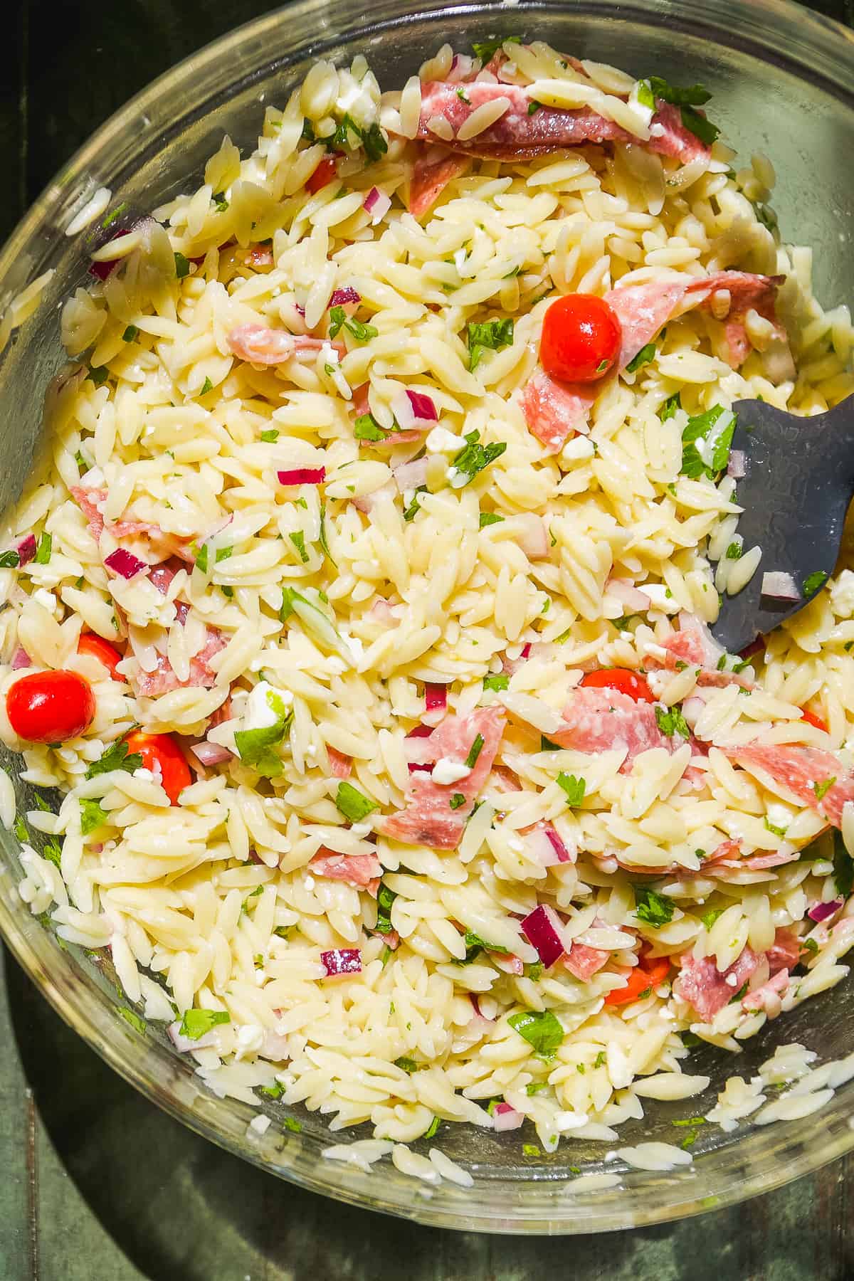 Overhead view of a large glass bowl with lemon orzo pasta with tomatoes and salami.