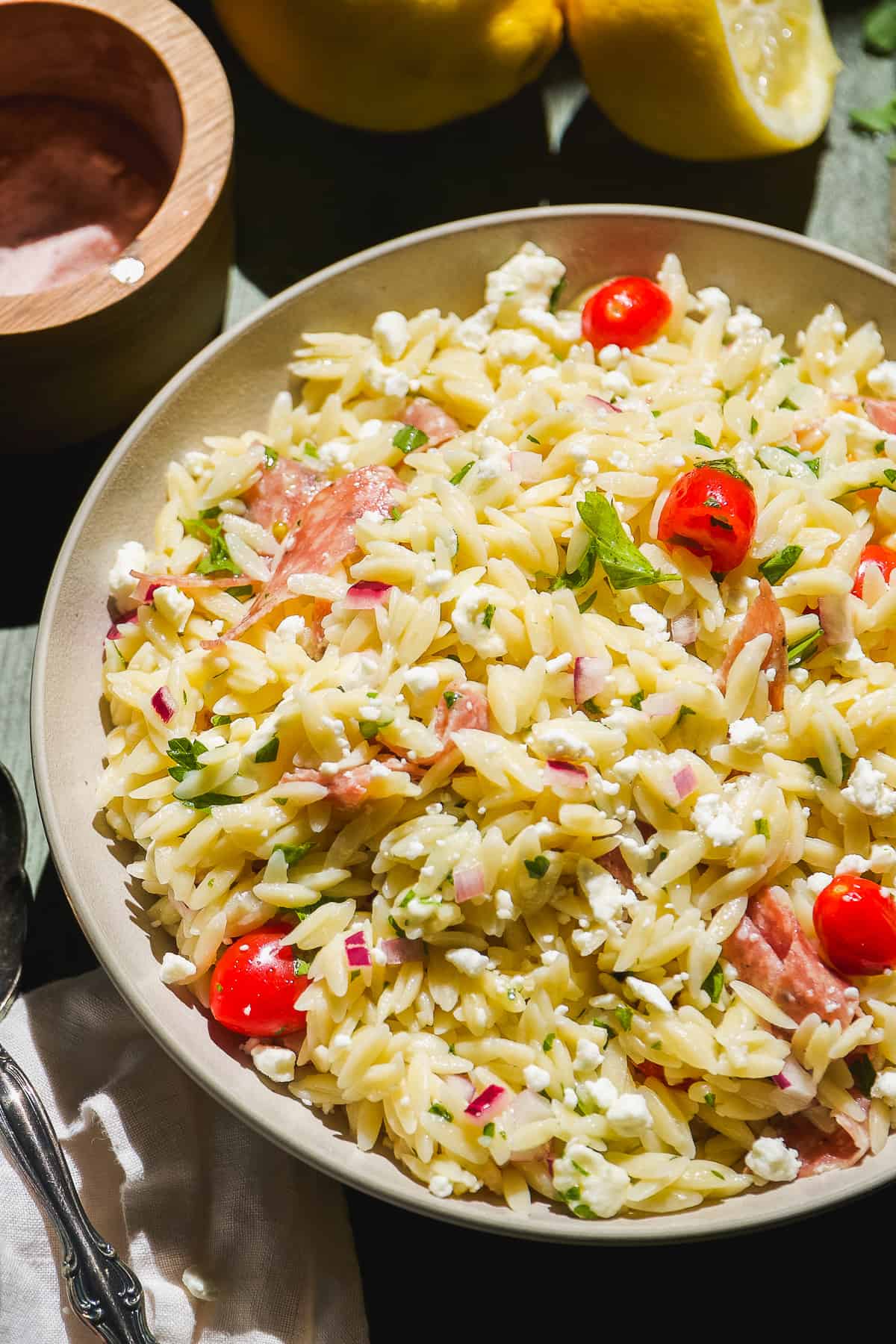 Dish with orzo pasta, tomatoes, and salami mixed with parsley dressing.