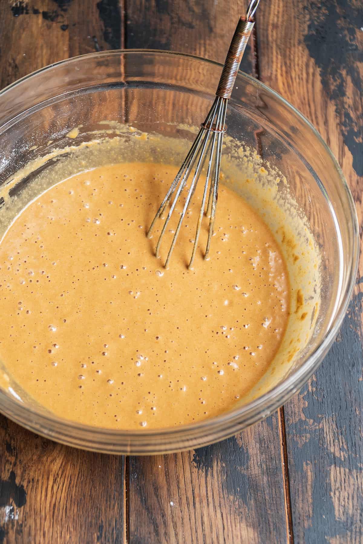 Oat flour cake batter in a large glass bowl with a whisk.