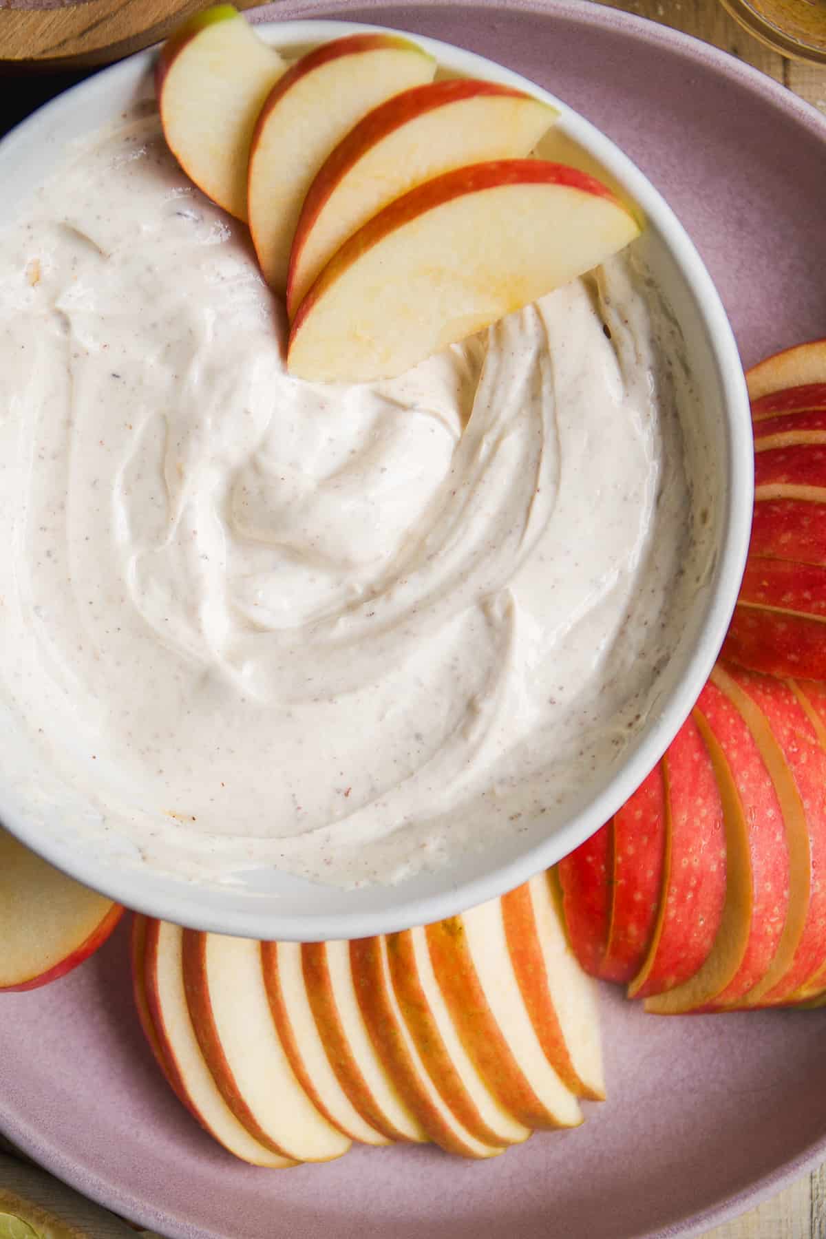 Apples cut into slices with a bowl of almond butter yogurt dip.